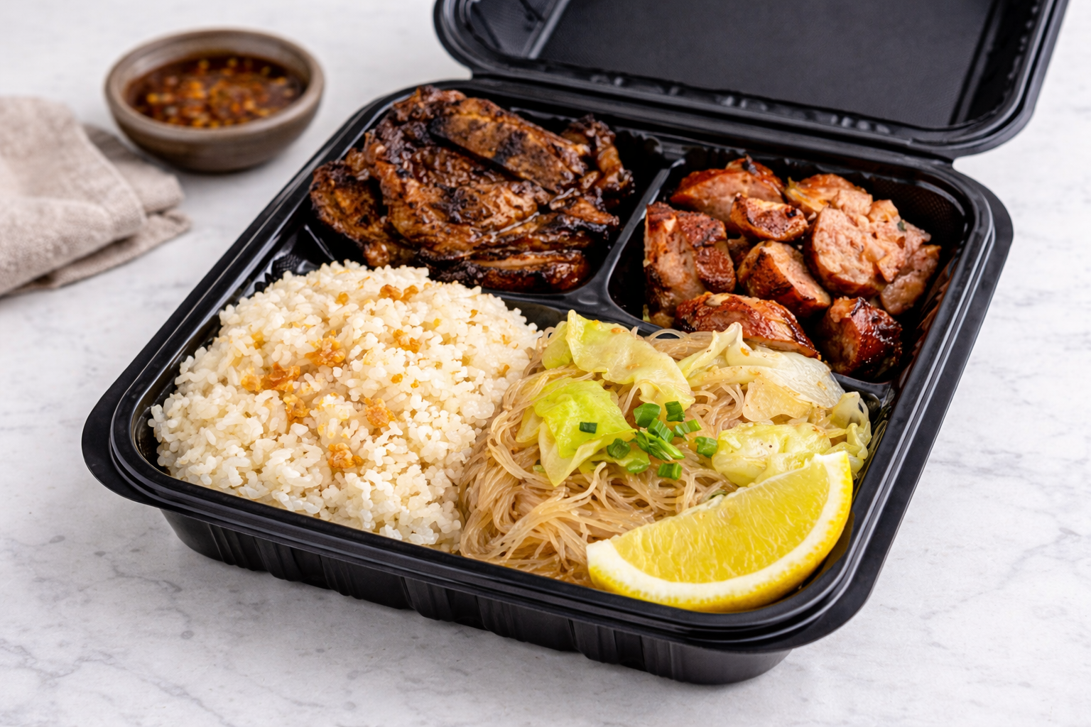 Bento box with bone-in short ribs, sliced pork jalapeño cheddar, garlic rice, and glass noodle pancit with cabbage and lemon wedge.